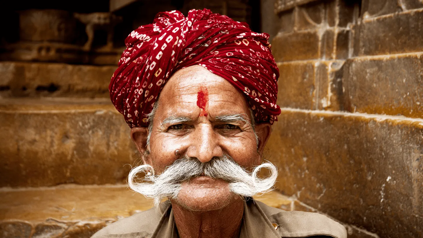 Portrait rapproché d'un homme indien âgé avec un tilak rouge sur le front devant un arrière-plan en pierre