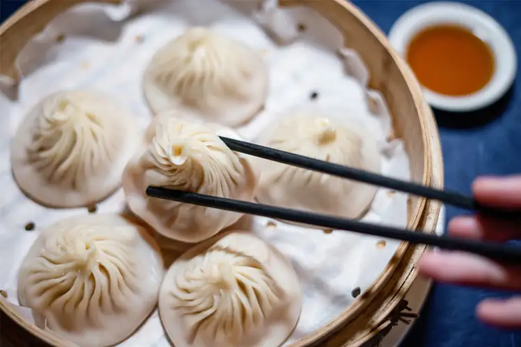 Panier en bambou garni de raviolis chinois faits main Xiaolongbao tenus avec des baguettes lors d'un atelier culinaire à Pékin.