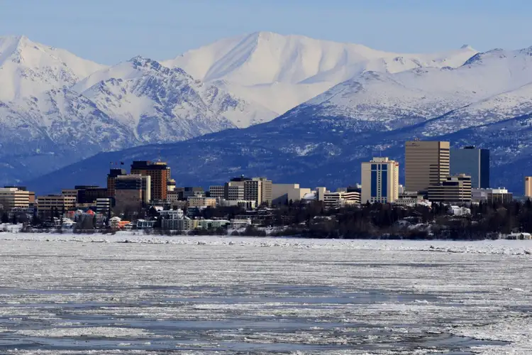 Vue sur la ville d'Anchorage et ses immeubles bordés par les eaux gelées avec les sommets enneigés des montagnes Chugach en arrière-plan