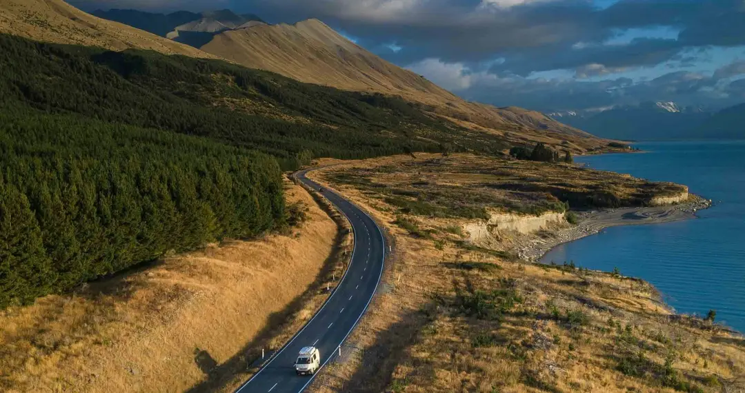 Van parcourant une route sinueuse longeant un lac en Nouvelle-Zélande