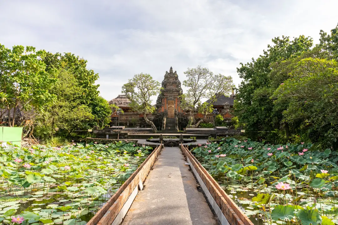 Voyage en Asie – Allée centrale menant au grand portail en pierre sculptée du temple Pura Taman Saraswati entouré de bassins remplis de lotus à Ubud à Bali.