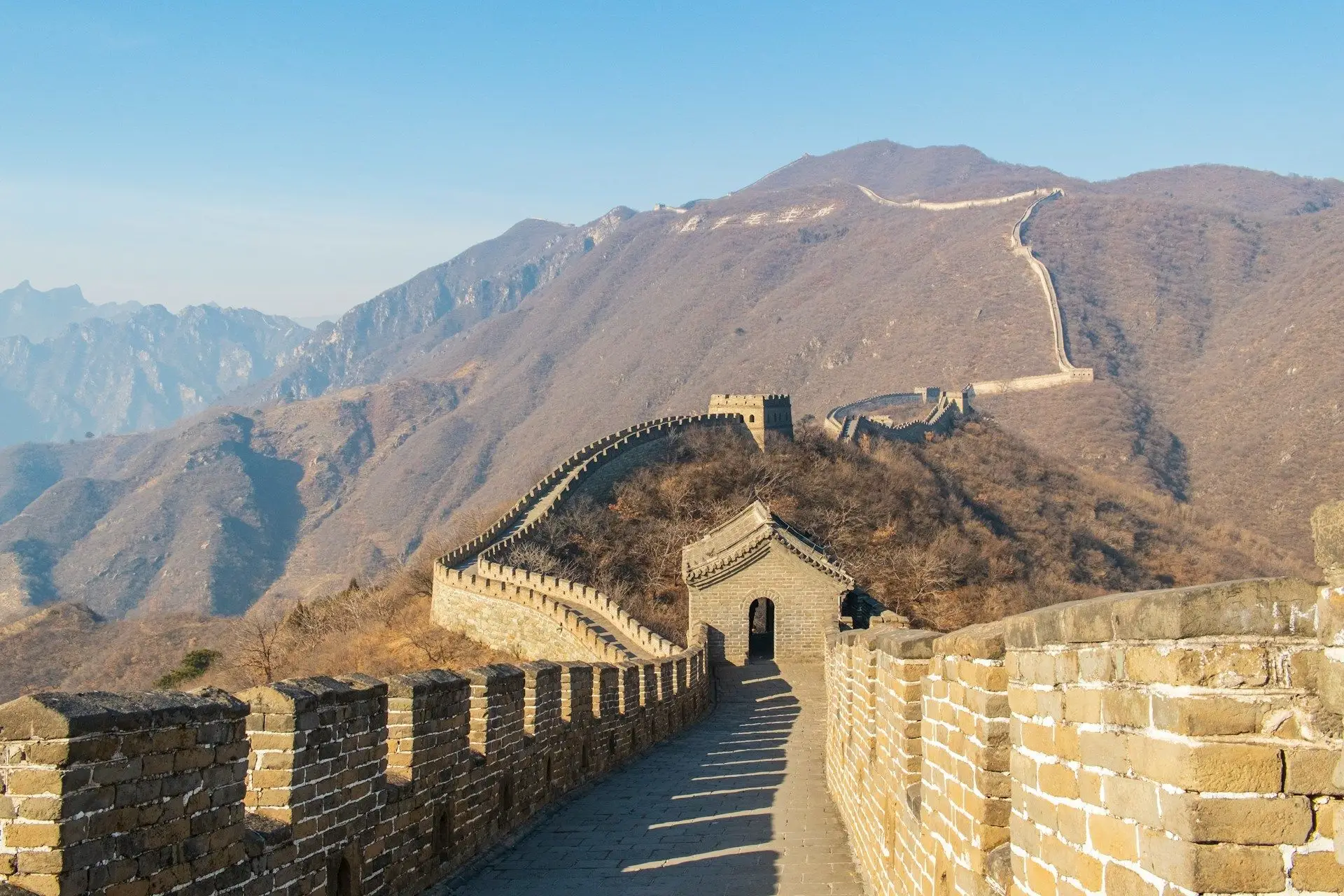 Vue de la Grande Muraille de Chine serpentant à travers les montagnes sous un ciel dégagé.
