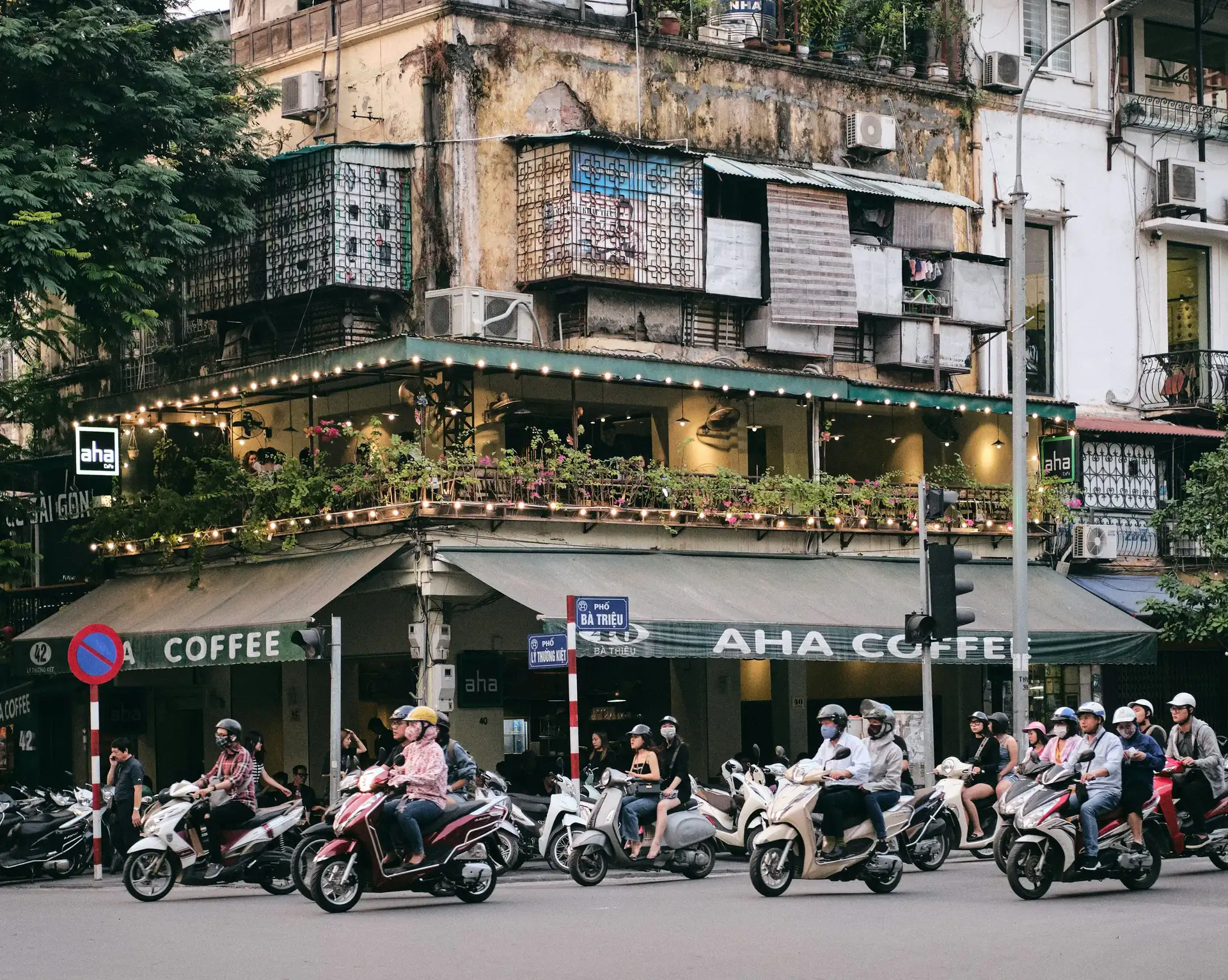 Transports au Vietnam – Circulation dynamique de scooters et voitures dans une rue de Hanoi devant un café colonial.