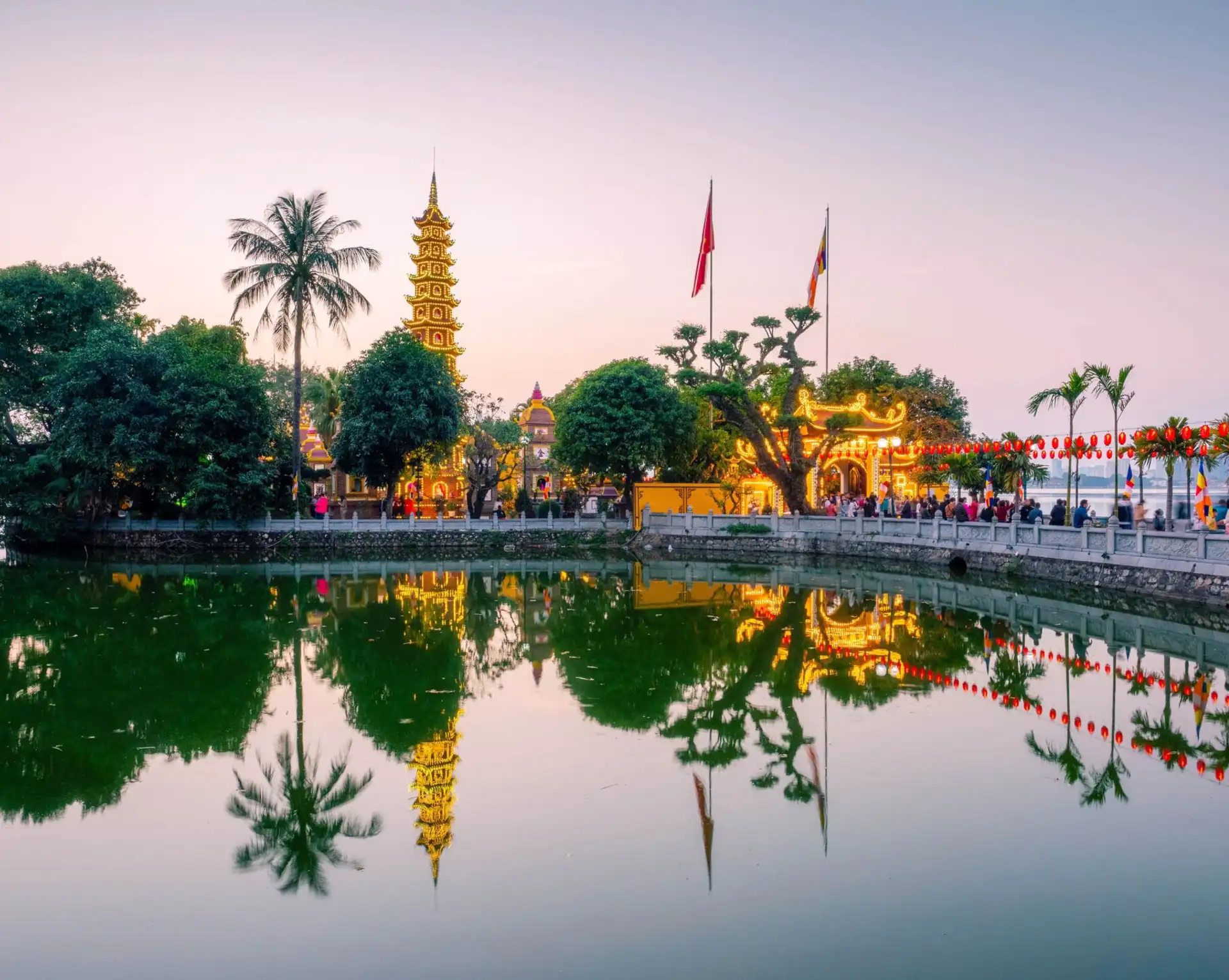 Une vue panoramique au crépuscule de la pagode Tran Quoc éclairée sur sa petite île, se reflétant sur les eaux calmes du lac de l'Ouest (Tay Ho) à Hanoi.