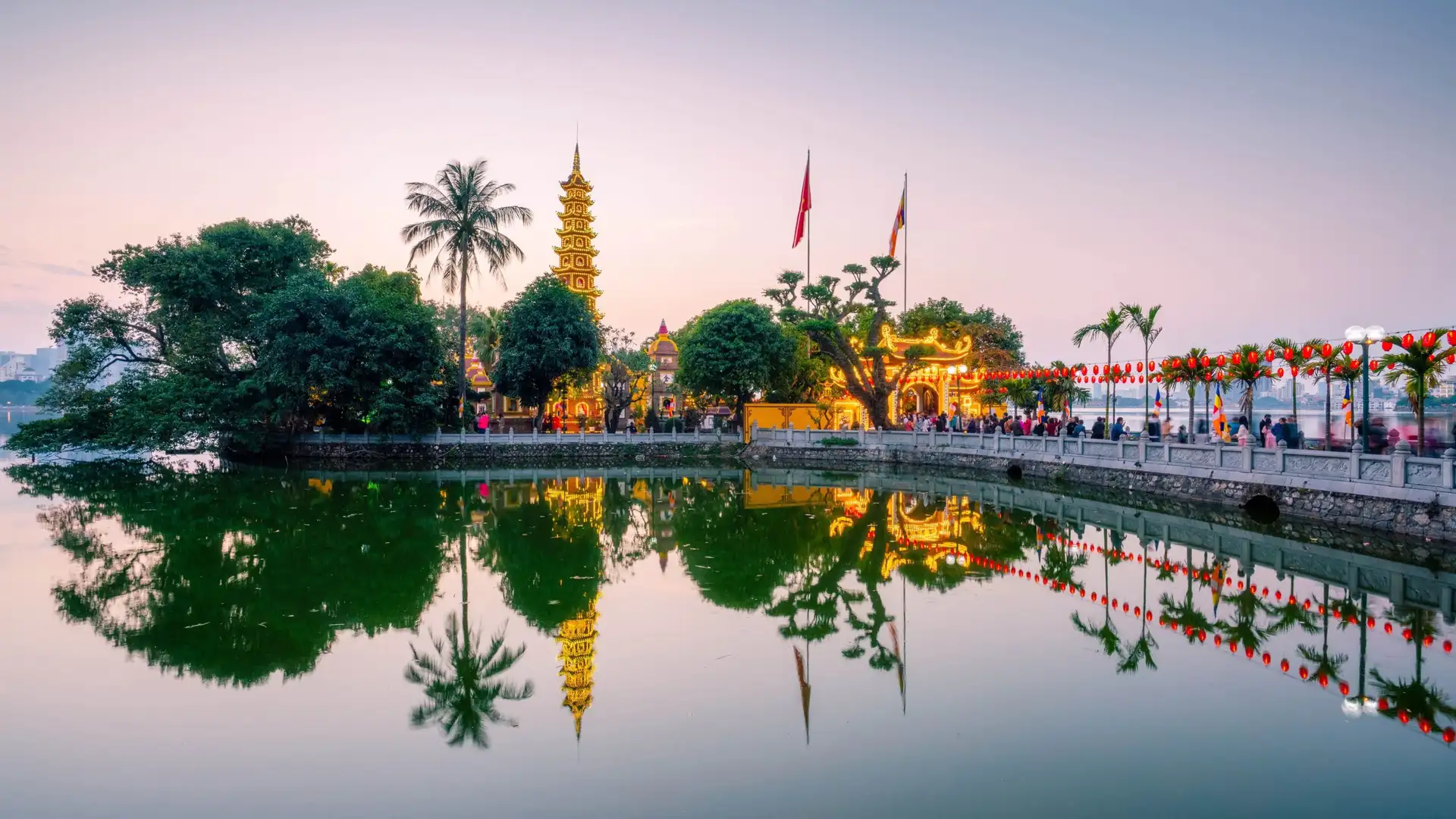Une vue panoramique au crépuscule de la pagode Tran Quoc éclairée sur sa petite île, se reflétant sur les eaux calmes du lac de l'Ouest (Tay Ho) à Hanoi.