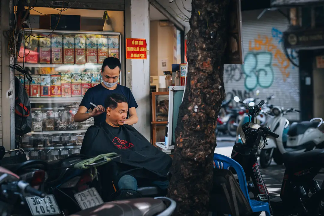 Coiffeur de rue en plein travail sur un trottoir animé du Vieux quartier de Hanoï, témoin de la vie quotidienne authentique.