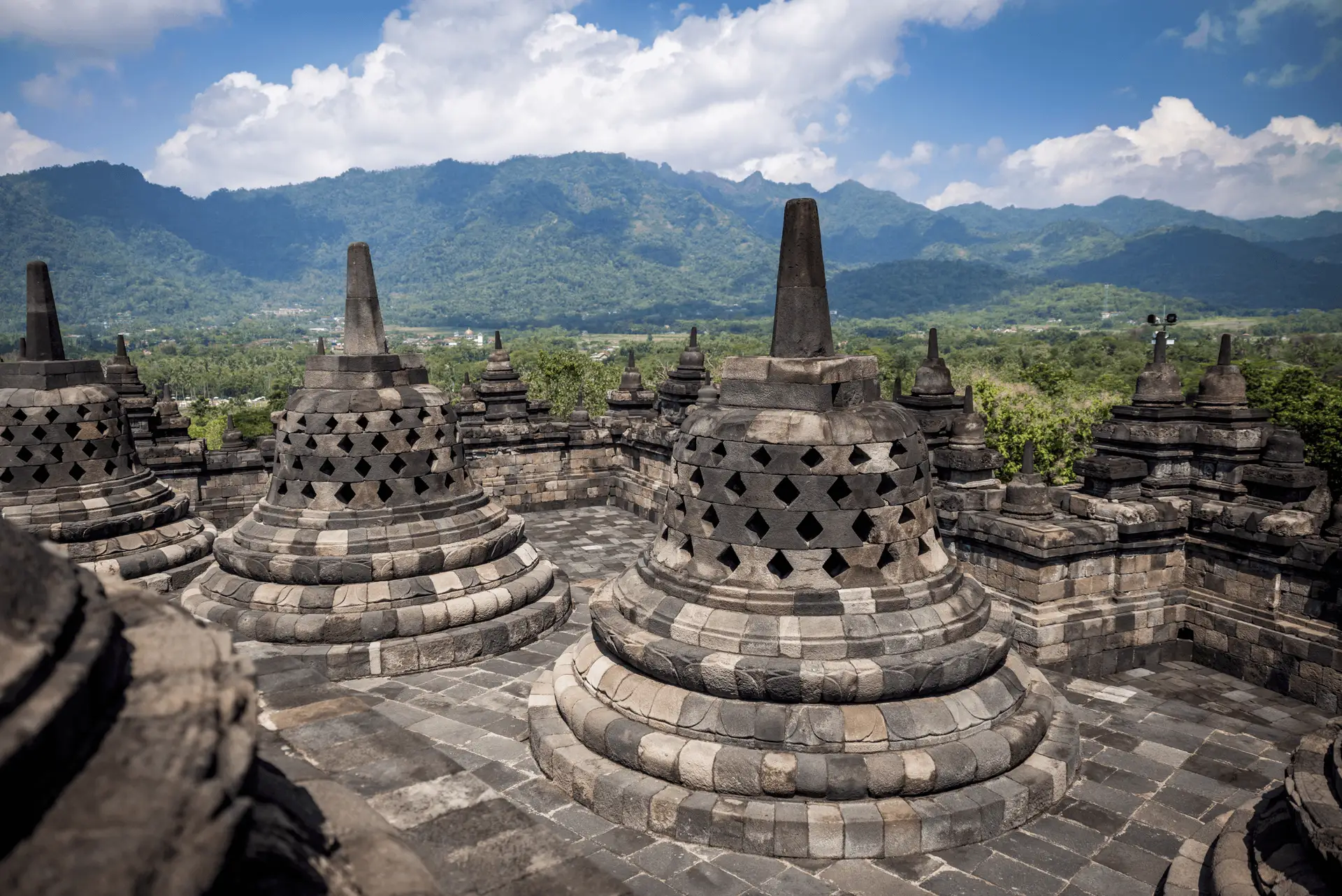 Voyage en Indonésie - stupas perforés au sommet du temple de Borobudur avec les volcans de Java en arrière-plan