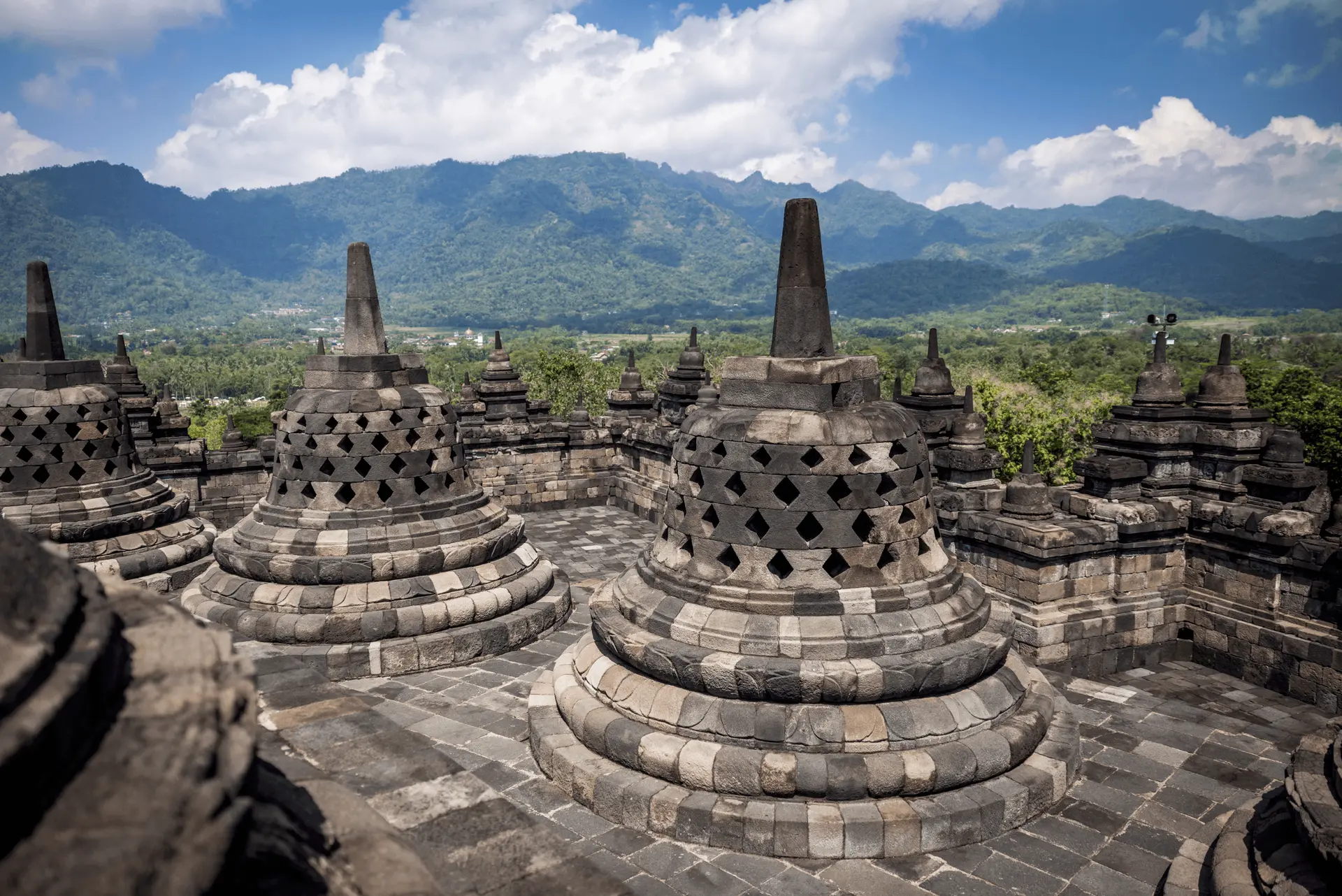 Voyage en Indonésie - stupas perforés au sommet du temple de Borobudur avec les volcans de Java en arrière-plan