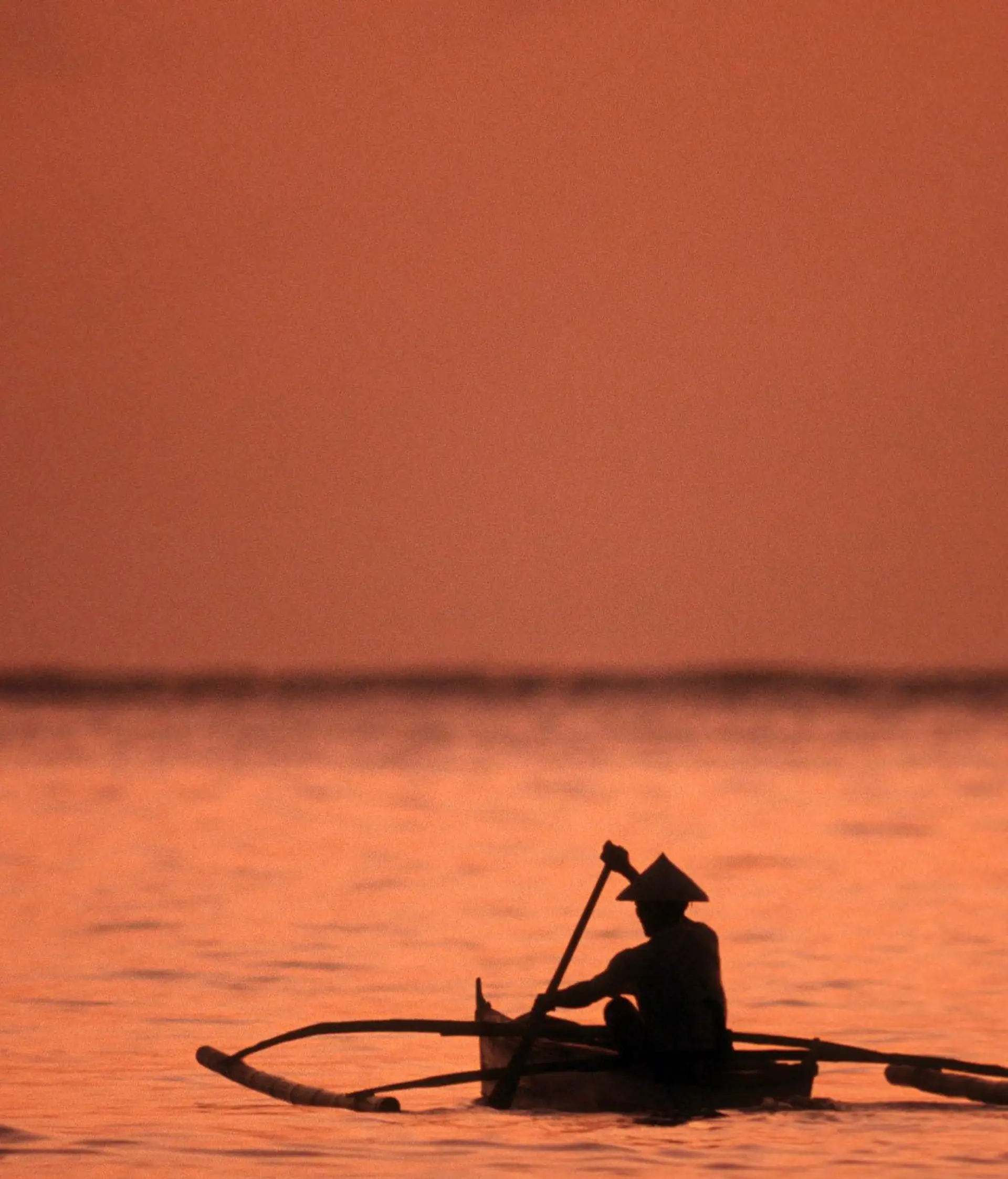 Coucher de soleil orangé sur le fleuve Mékong avec des barques traditionnelles amarrées à Luang Prabang au Laos.