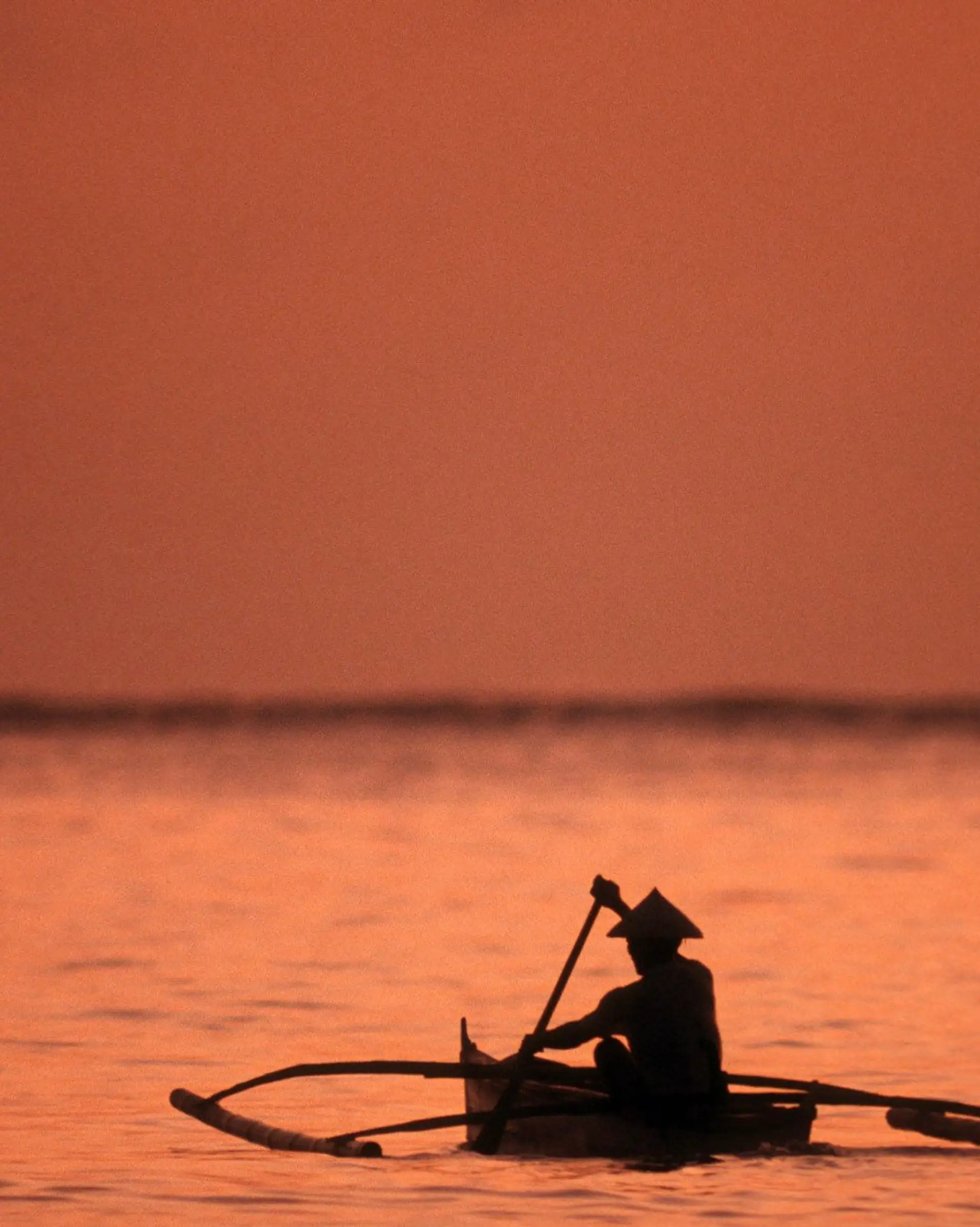 Coucher de soleil orangé sur le fleuve Mékong avec des barques traditionnelles amarrées à Luang Prabang au Laos.