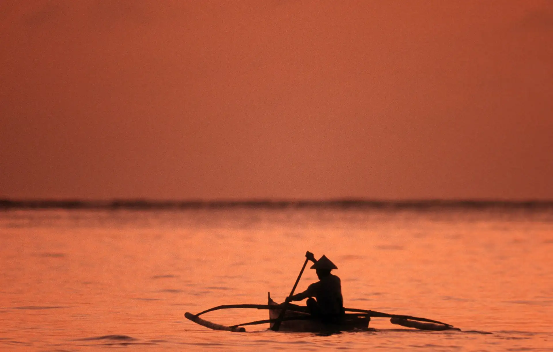 Coucher de soleil orangé sur le fleuve Mékong avec des barques traditionnelles amarrées à Luang Prabang au Laos.