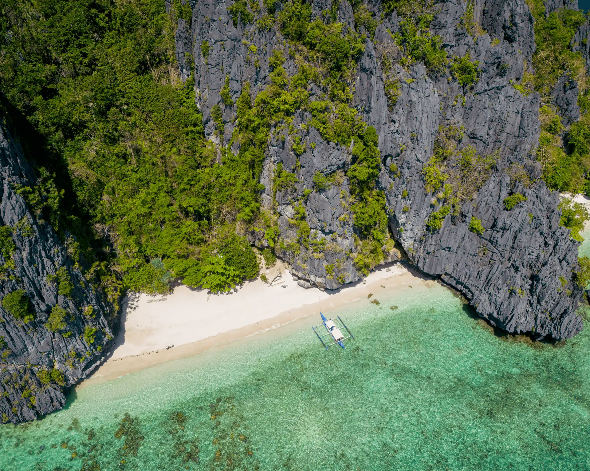 Vue aérienne d'une plage de sable blanc bordée d'eaux turquoises et de falaises calcaires impressionnantes sur Shimizu Island à El Nido.