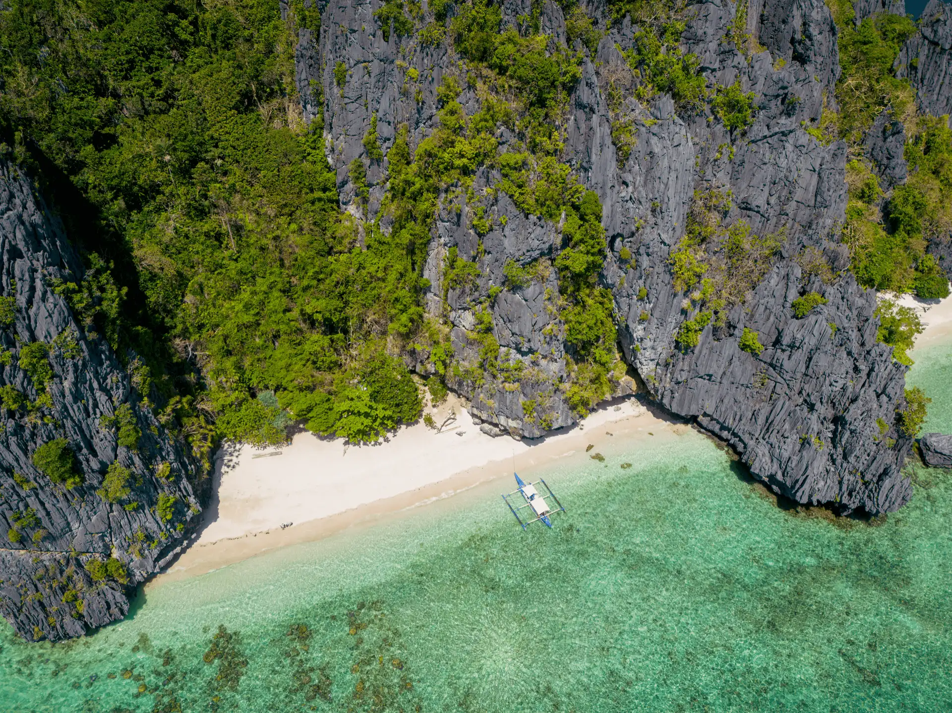 Vue aérienne d'une plage de sable blanc bordée d'eaux turquoises et de falaises calcaires impressionnantes sur Shimizu Island à El Nido.