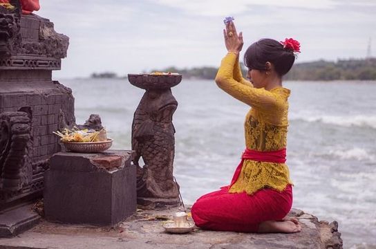Voyage en Asie — Femme balinaise en prière avec offrandes sur une plate-forme de temple à Bali : geste de dévotion et ambiance recueillie.