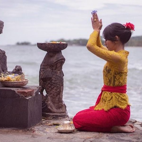 Voyage en Asie — Femme balinaise en prière avec offrandes sur une plate-forme de temple à Bali : geste de dévotion et ambiance recueillie.
