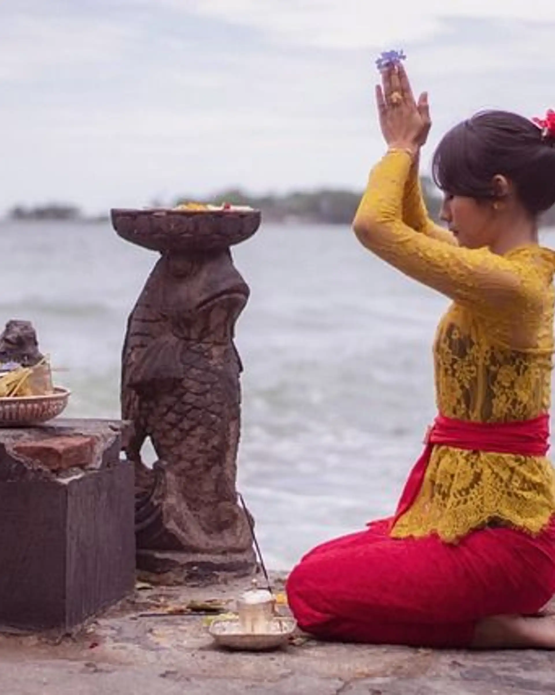 Voyage en Asie — Femme balinaise en prière avec offrandes sur une plate-forme de temple à Bali : geste de dévotion et ambiance recueillie.