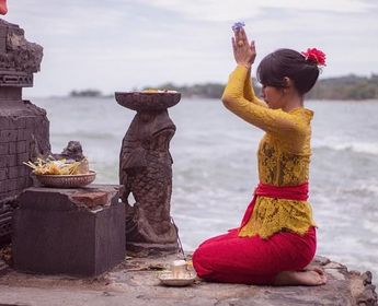 Voyage en Asie — Femme balinaise en prière avec offrandes sur une plate-forme de temple à Bali : geste de dévotion et ambiance recueillie.