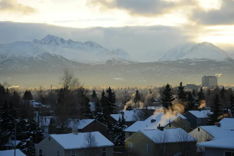 Vue sur les toits et conifères d'Anchorage avec les imposantes montagnes enneigées en arrière-plan sous un ciel d'hiver voilé en Alaska