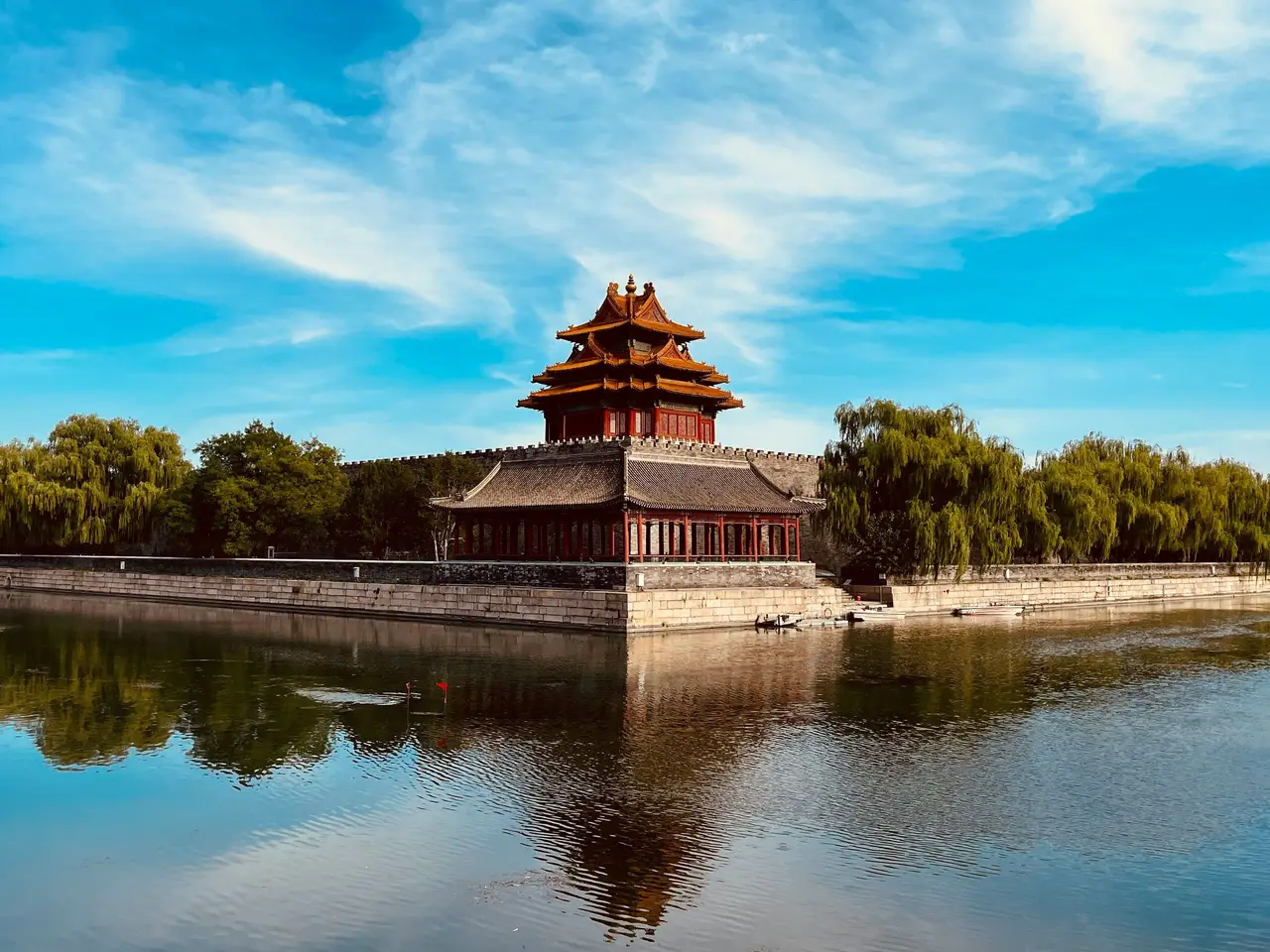 Une tour d'angle traditionnelle de la Cité Interdite avec ses toits superposés se reflétant sur l'eau des douves sous un ciel bleu à Pékin.
