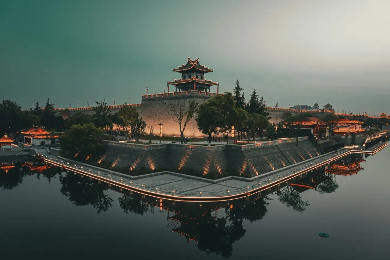 Les remparts historiques en pierre de Xi'an et une tour de guet traditionnelle illuminée se reflétant sur l'eau des douves au crépuscule.