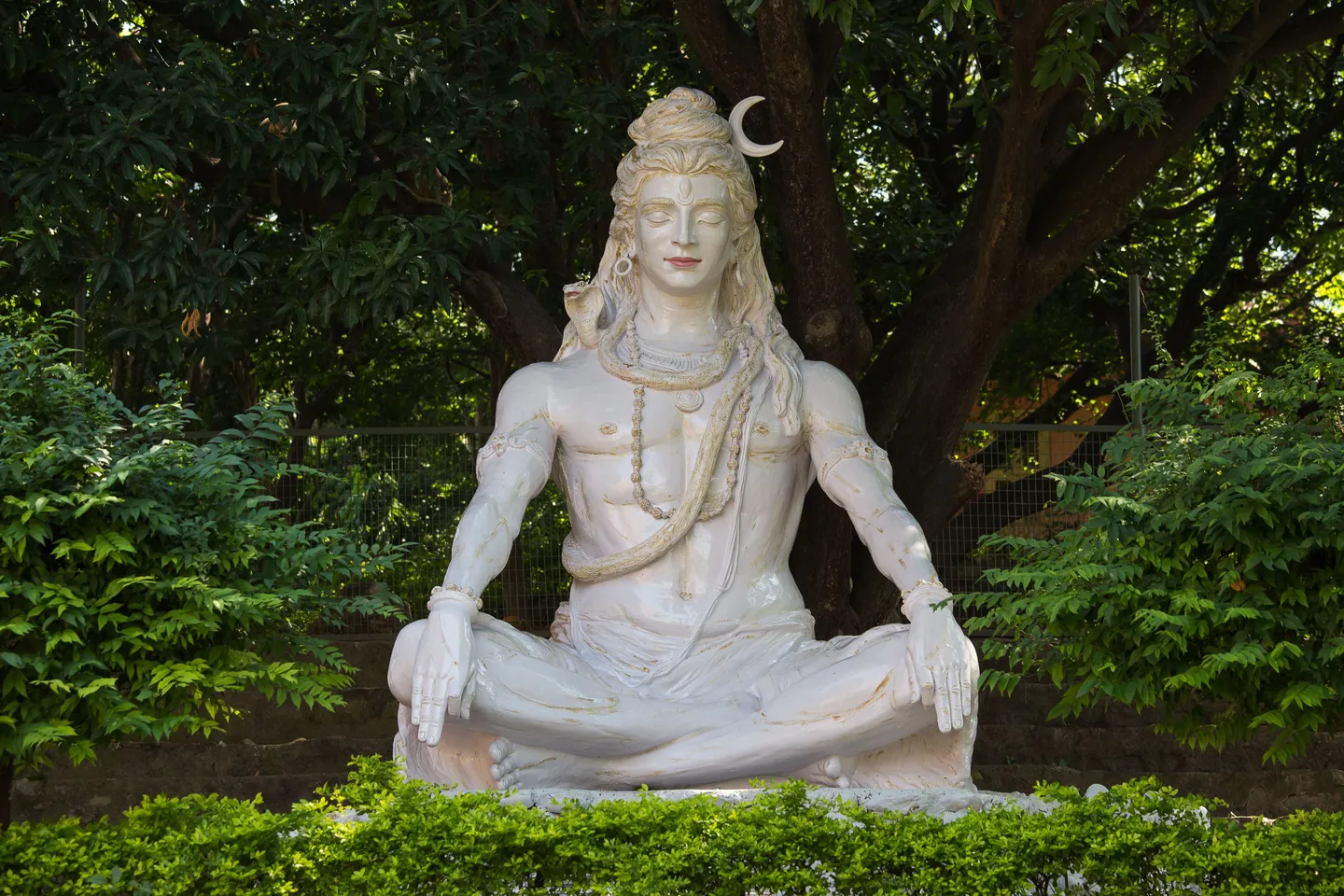 voyage en Inde - Statue blanche de Shiva en posture de yoga nichée dans un écrin de verdure.