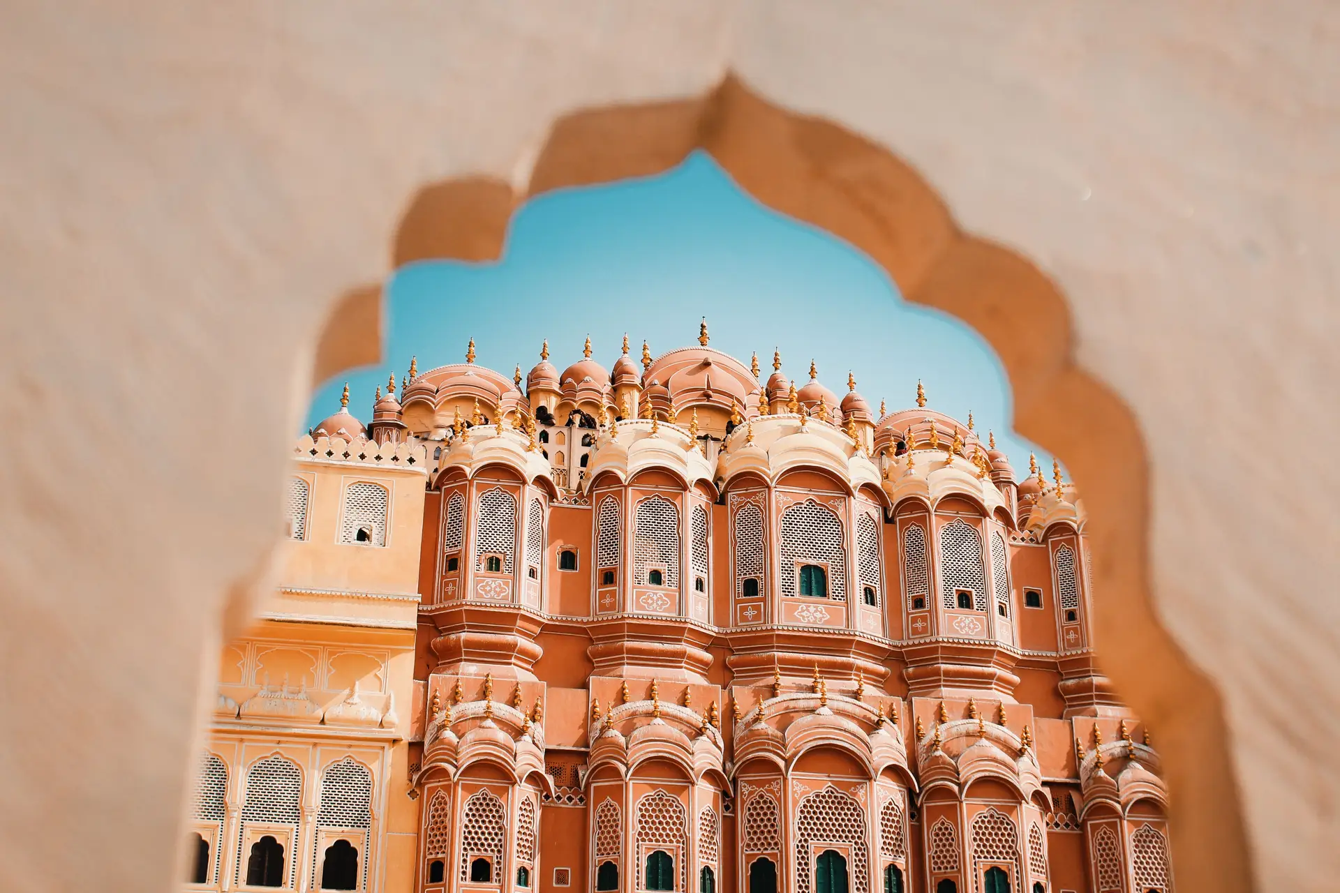 La façade sculptée en grès rose du Hawa Mahal (Palais des Vents) vue à travers une arche architecturale traditionnelle à Jaipur.