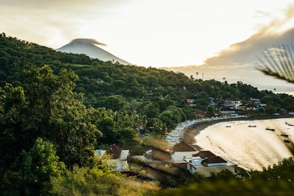 Voyage en Asie — Vue panoramique de la baie d'Amed à Bali : plage, végétation luxuriante et volcan à l'horizon au lever/coucher du soleil.