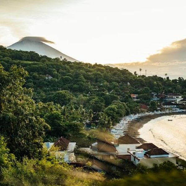 Voyage en Asie — Vue panoramique de la baie d'Amed à Bali : plage, végétation luxuriante et volcan à l'horizon au lever/coucher du soleil.