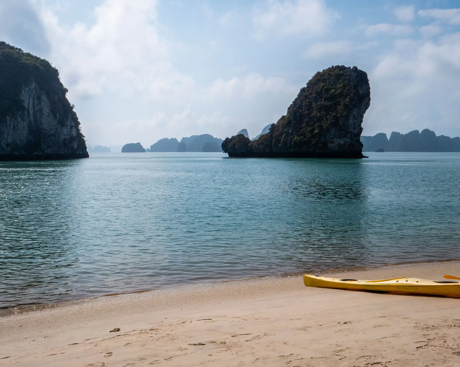 pitons rocheux karstiques emblematiques de la baie d halong s elevant au dessus de l eau calme depuis une plage de sable