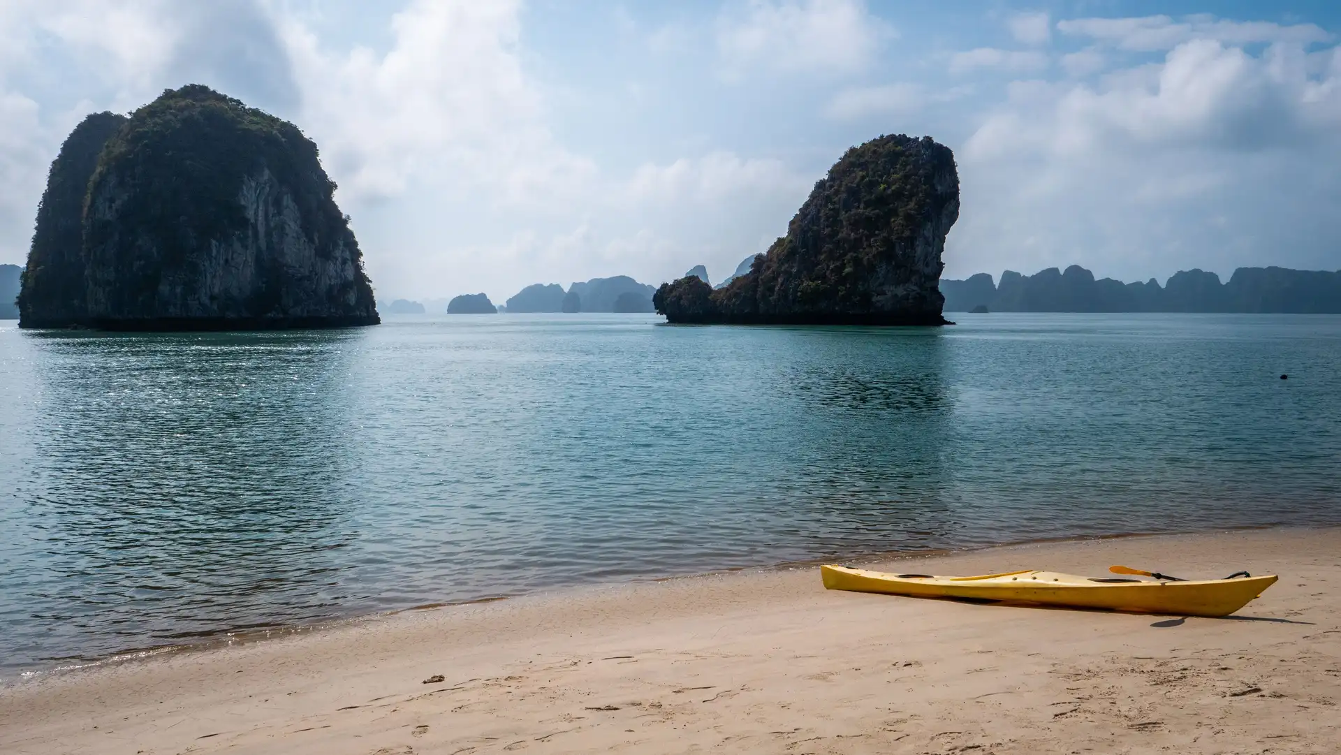 pitons rocheux karstiques emblematiques de la baie d halong s elevant au dessus de l eau calme depuis une plage de sable