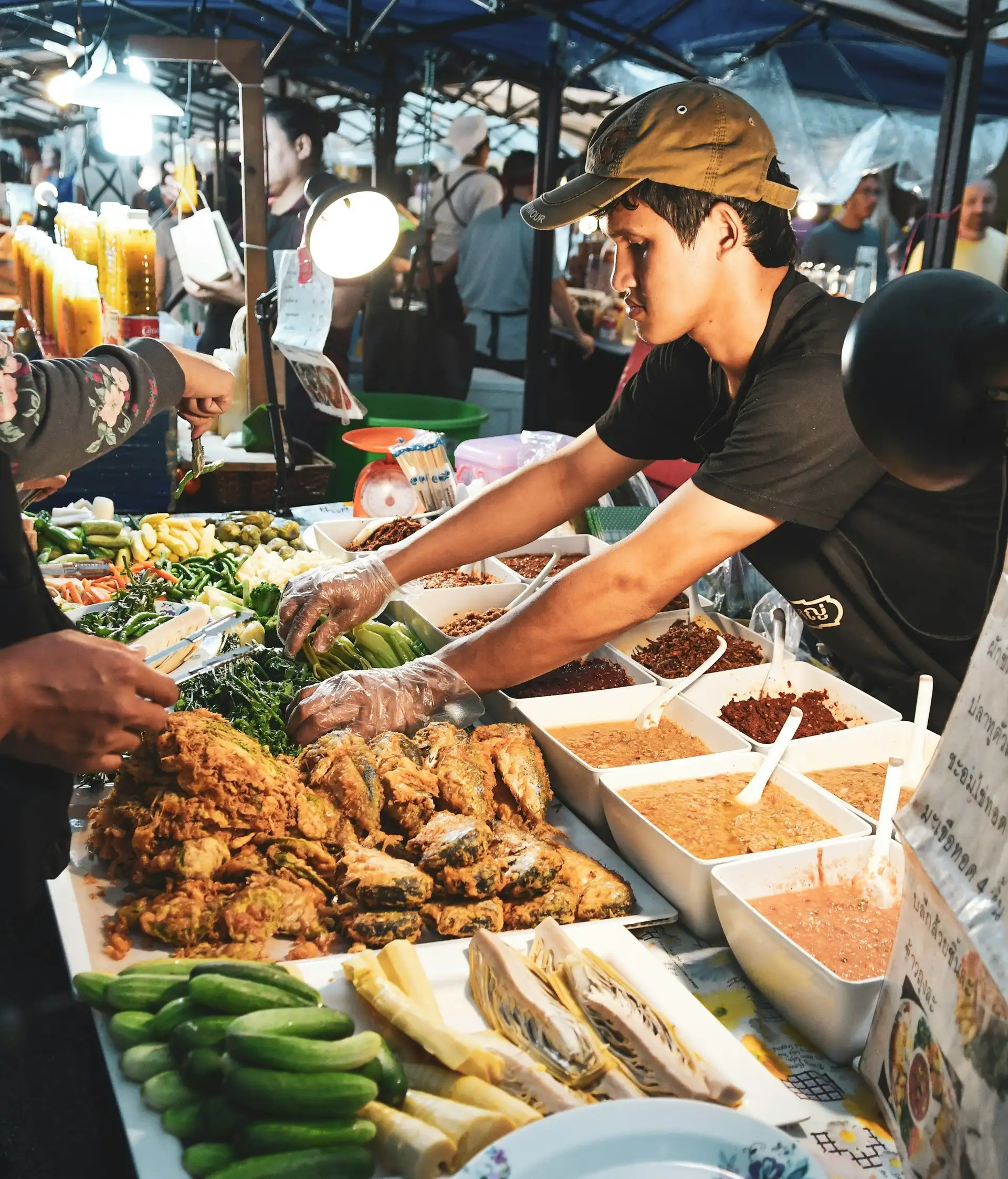 Un stand de street food animé dans un marché de nuit local à Bali, où un cuisinier prépare des plats traditionnels balinais au milieu d'étals de nourriture.