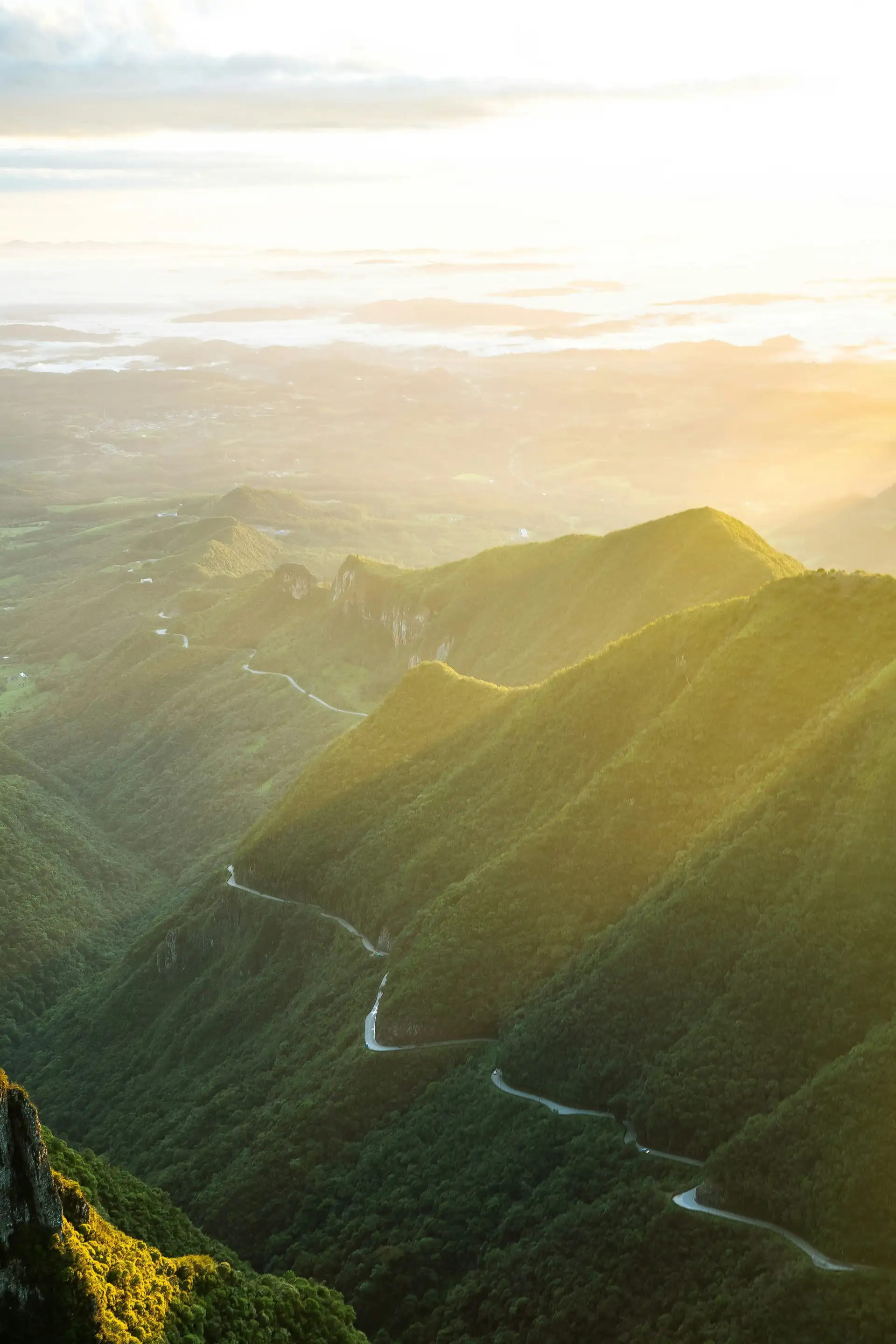 Voyage au Brésil – Des montagnes verdoyantes et des collines abruptes éclairées par la lumière du soleil couchant à travers la brume.