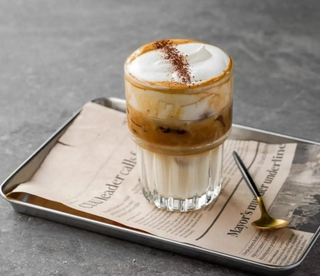 Un verre de café salé vietnamien Cà Phê Muối, composé d'un shot de café surmonté d'une onctueuse crème salée saupoudrée de cacao.