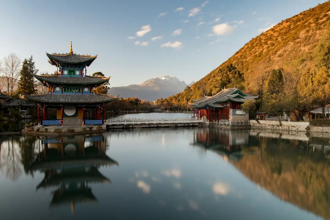 pagode traditionnelle chinoise se refletant sur un etang paisible face a une colline boisee a l automne sous un ciel degage