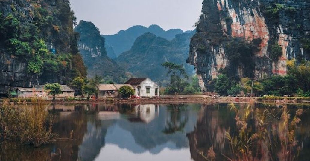 Travel in Asia - A small building on the edge of the water surrounded by dramatic cliffs in Ninh Binh, Vietnam