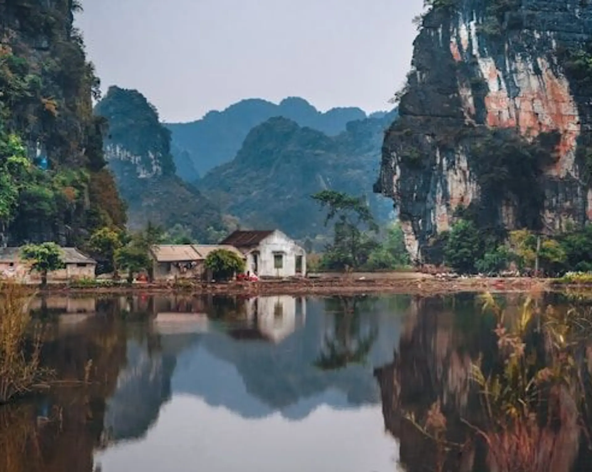 Travel in Asia - A small building on the edge of the water surrounded by dramatic cliffs in Ninh Binh, Vietnam