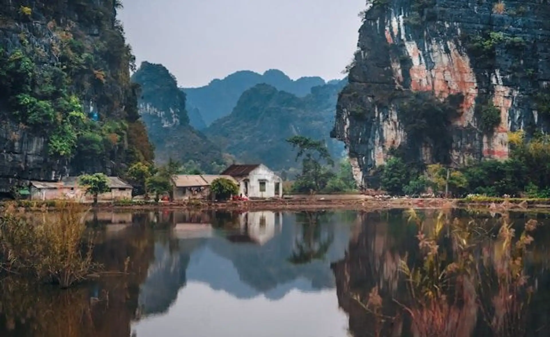 Travel in Asia - A small building on the edge of the water surrounded by dramatic cliffs in Ninh Binh, Vietnam
