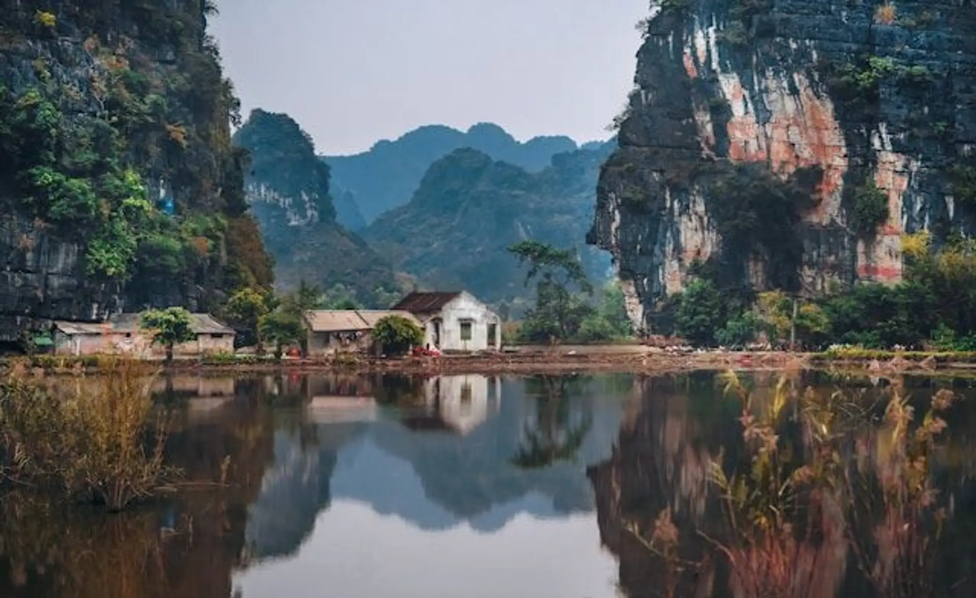 Travel in Asia - A small building on the edge of the water surrounded by dramatic cliffs in Ninh Binh, Vietnam