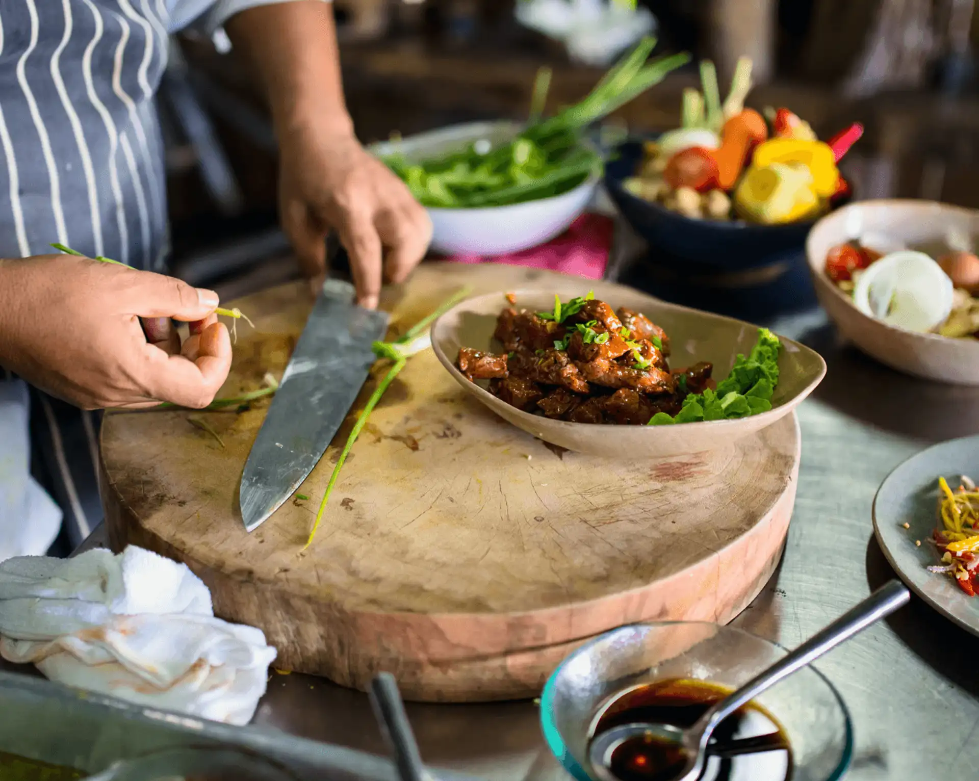 chef cuisinier en tablier raye decoupant des herbes fraiches et legumes locaux sur une grande planche en bois lors d un cours de cuisine traditionnelle au cambodge