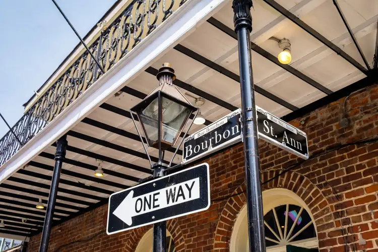 Panneau indiquant l'angle des rues Bourbon Street et St. Ann devant une façade en brique et un balcon en fer forgé à La Nouvelle-Orléans