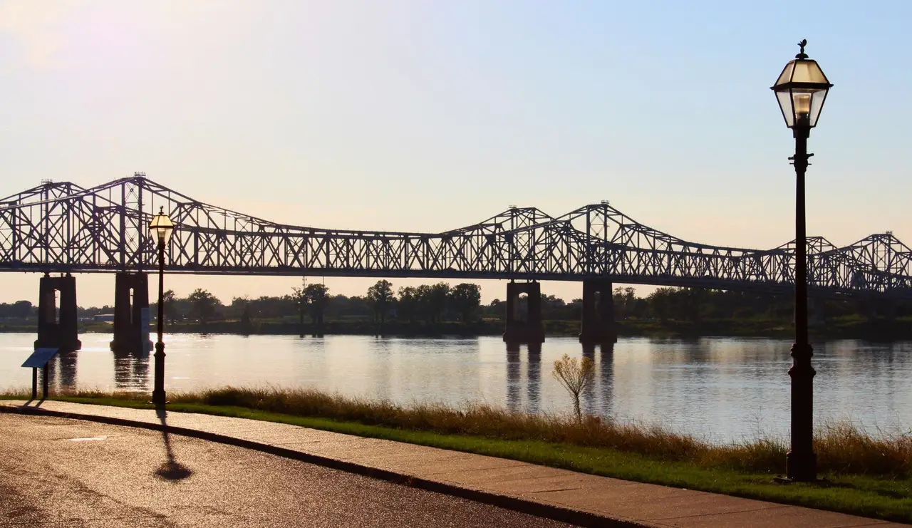 Pont métallique traversant le fleuve Mississippi vu depuis les berges aménagées de Natchez avec un lampadaire au premier plan