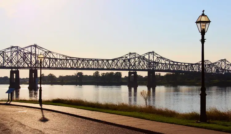 Pont métallique traversant le fleuve Mississippi vu depuis les berges aménagées de Natchez avec un lampadaire au premier plan