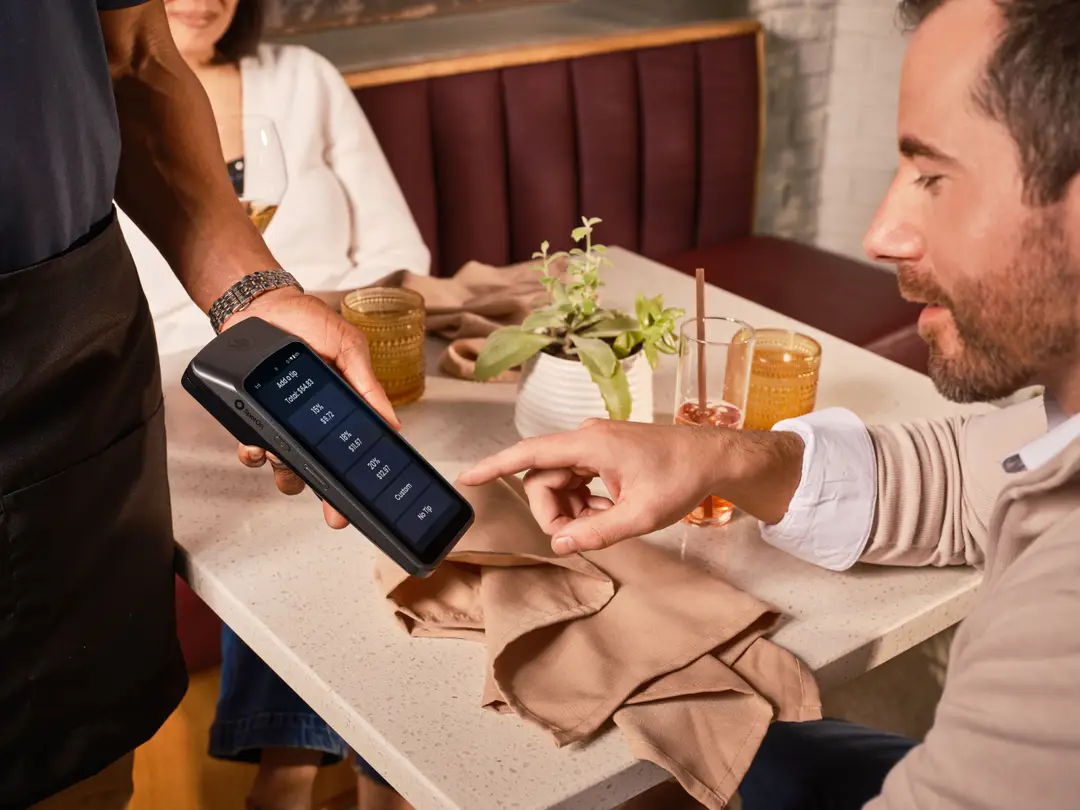 Dans un restaurant décontracté, un client utilise un terminal de point de vente portable pour laisser un pourboire numérique.