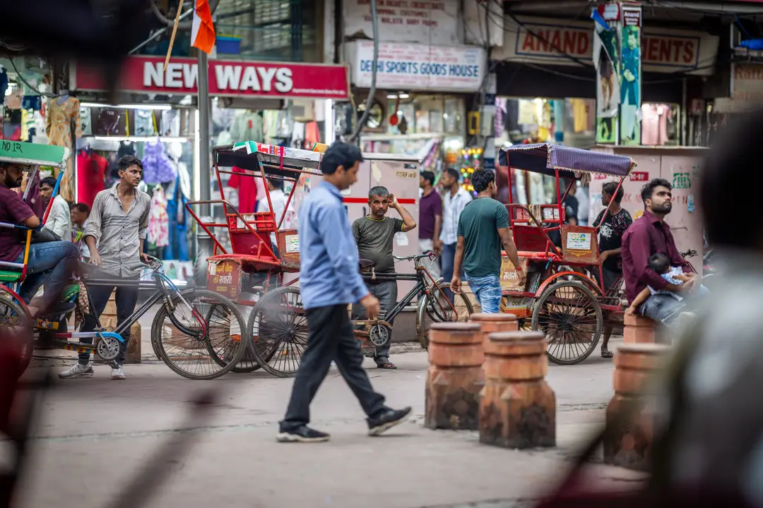 Une scène de rue animée et colorée à Chandni Chowk avec des passants et plusieurs cyclo-pousses (rickshaws) traditionnels stationnés devant des boutiques locales à Old Delhi en Inde.