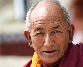 Voyage en Asie — Portrait d’un moine âgé à Leh, vêtu de robes bordeaux et orange, le visage éclairé par une lumière naturelle douce au cœur du Ladakh.