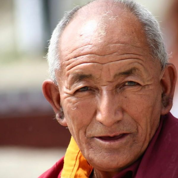 Voyage en Asie — Portrait d’un moine âgé à Leh, vêtu de robes bordeaux et orange, le visage éclairé par une lumière naturelle douce au cœur du Ladakh.