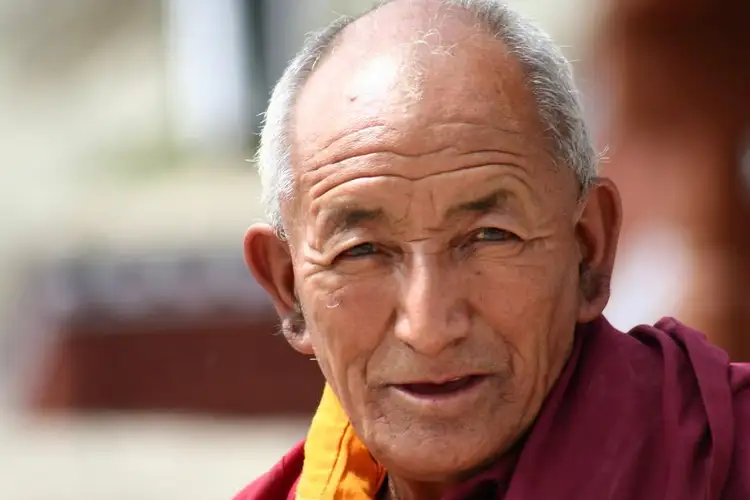 Voyage en Asie — Portrait d’un moine âgé à Leh, vêtu de robes bordeaux et orange, le visage éclairé par une lumière naturelle douce au cœur du Ladakh.