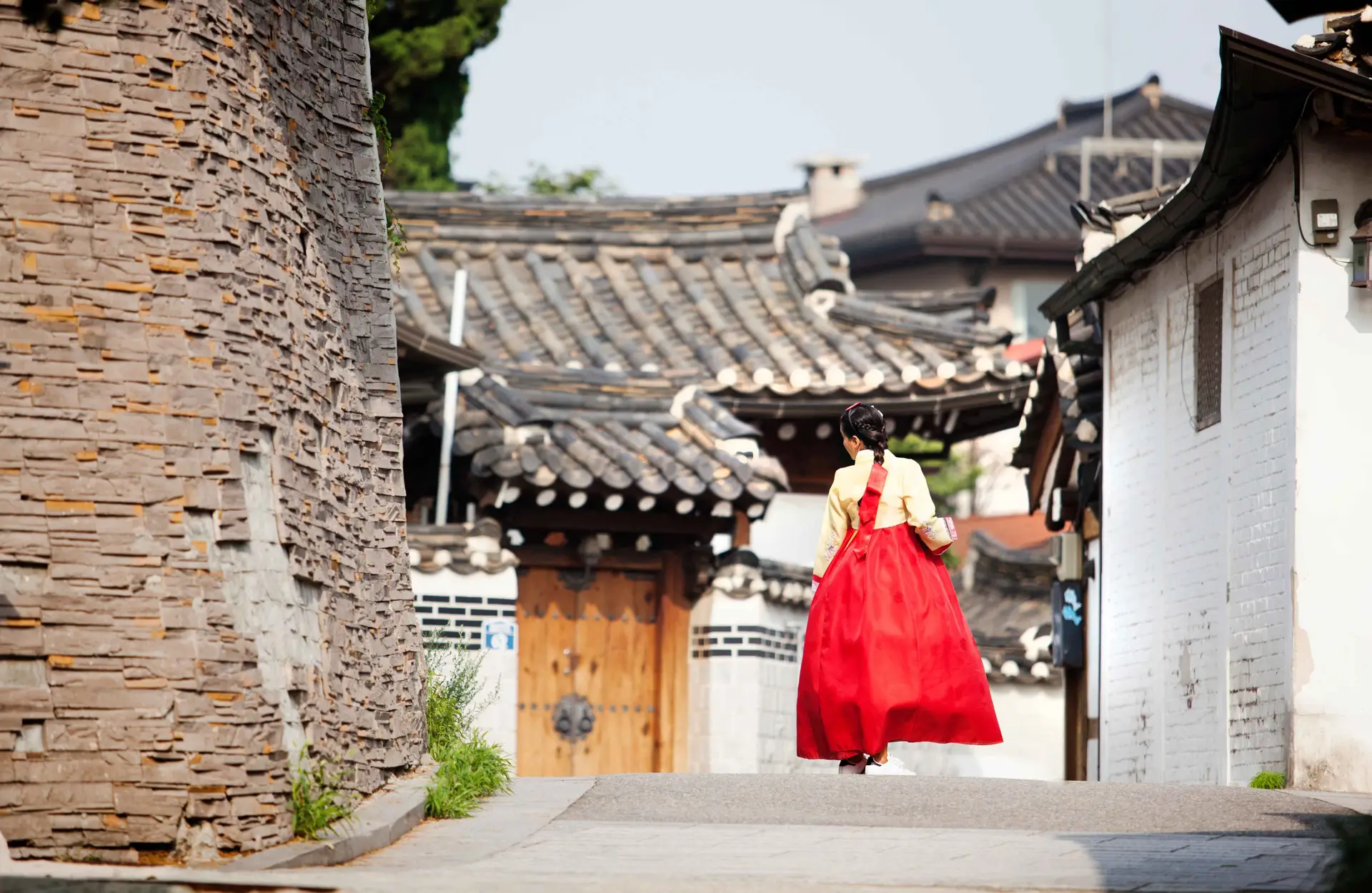 Une personne en hanbok traditionnel marchant dans une ruelle pittoresque bordée de maisons traditionnelles coréennes (hanoks) à Jeonju.