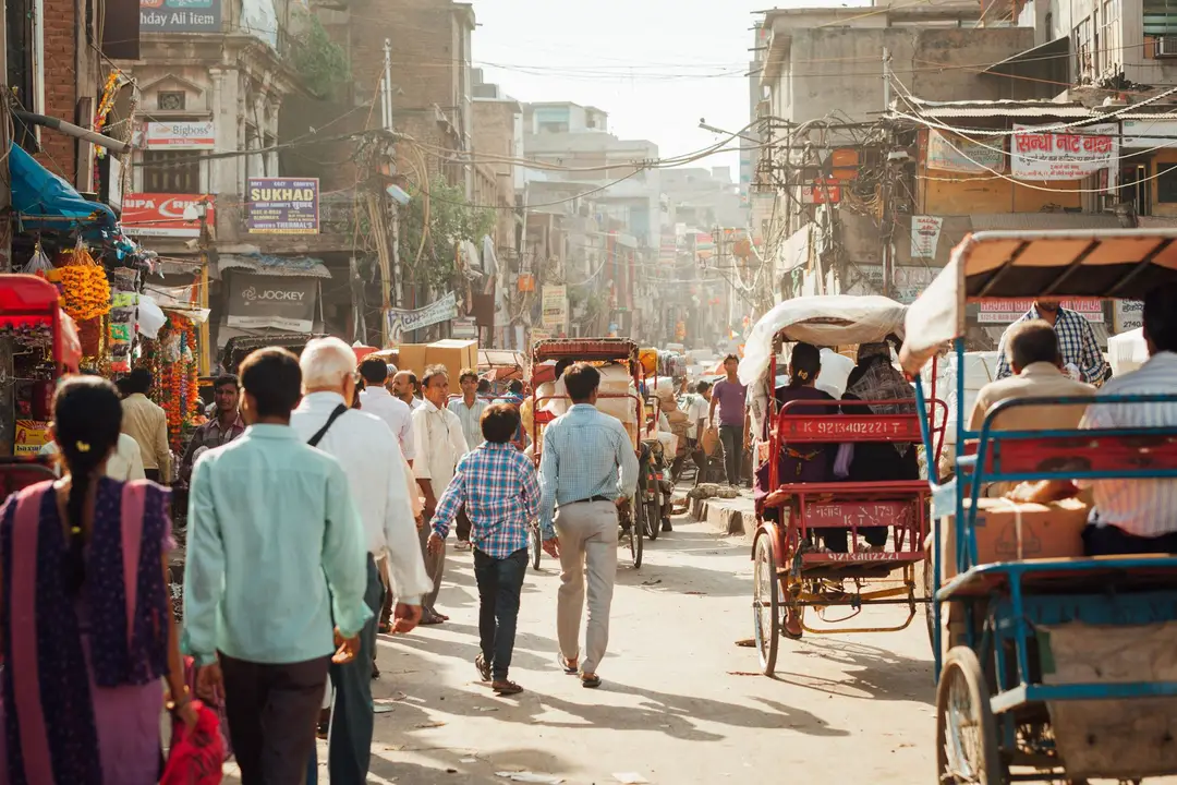 Passants et tuk-tuks circulant dans une rue animée bordée d'échoppes à Delhi.