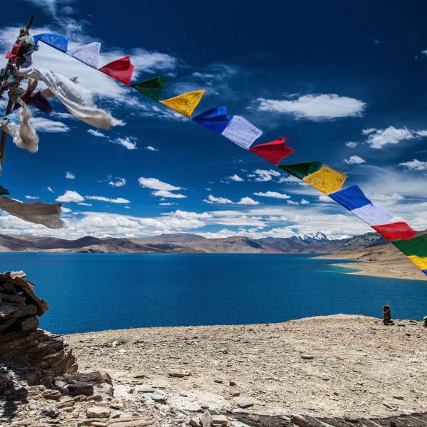 Voyage en Asie — Lac turquoise au Ladakh à Korzok Phu, entouré de montagnes désertiques et de drapeaux de prière bouddhistes tibétains.